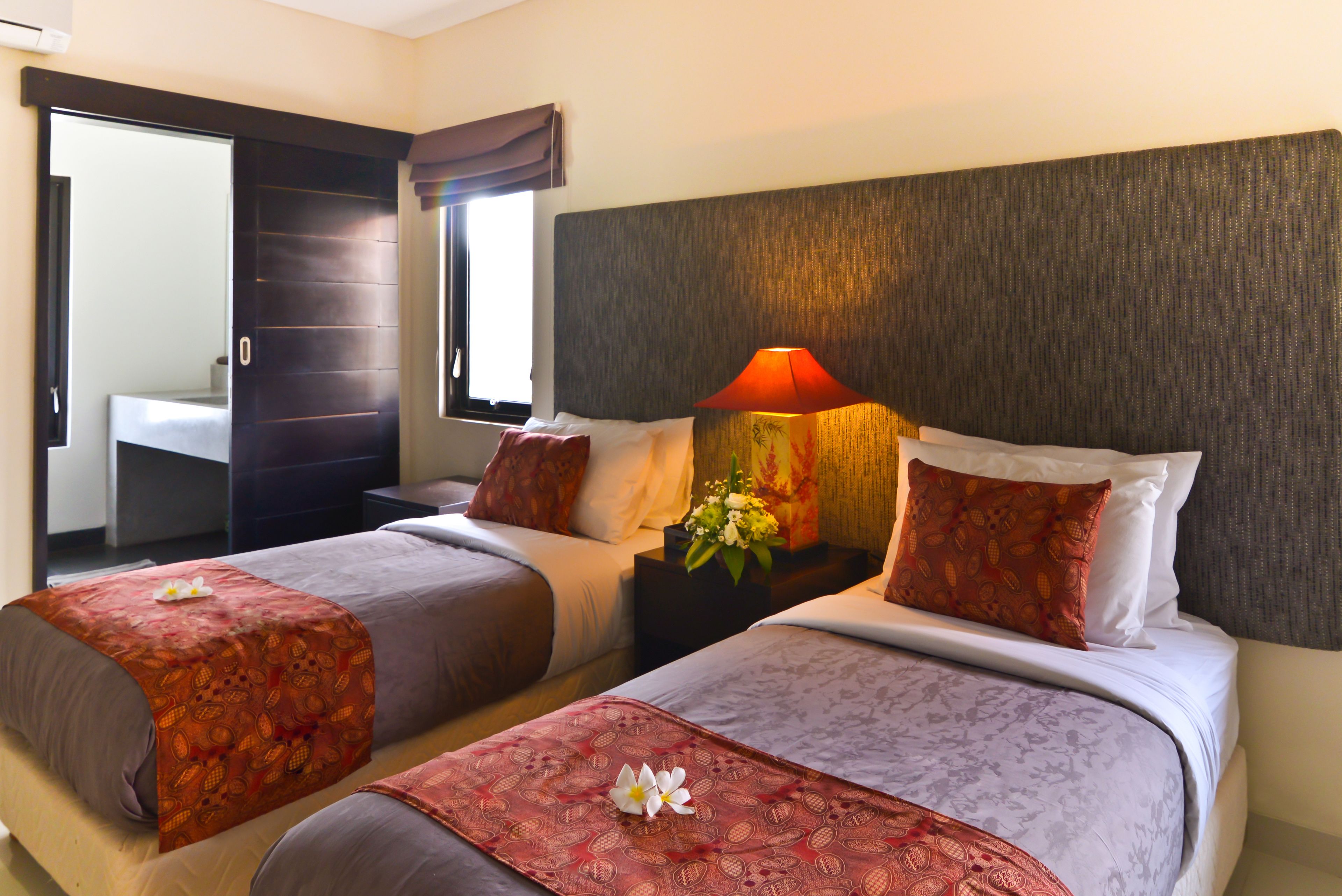 A hotel room with two beds, a nightstand with a lamp, and a window with curtains.