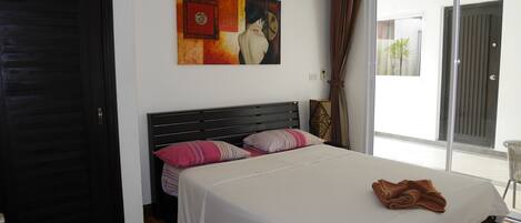 A bedroom with a large bed, a painting on the wall, and a sliding glass door to the outside.