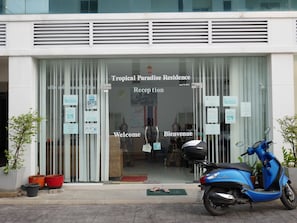 A building entrance with a sign reading "Tropical Paradise Residence Reception" and a blue scooter parked in front. - Tropical Paradise Residence (Koh Samui)