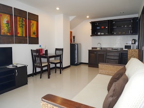 A modern living room with a sofa, a dining table with chairs, a TV, and a kitchen area with cabinets and a microwave.