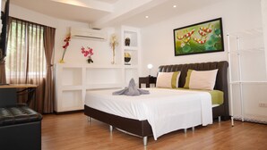 Ein modernes Schlafzimmer mit einem großen Bett, einem Schreibtisch und einem Stuhl. An der Wand hängt ein Gemälde, über dem Bett befindet sich eine Klimaanlage.
