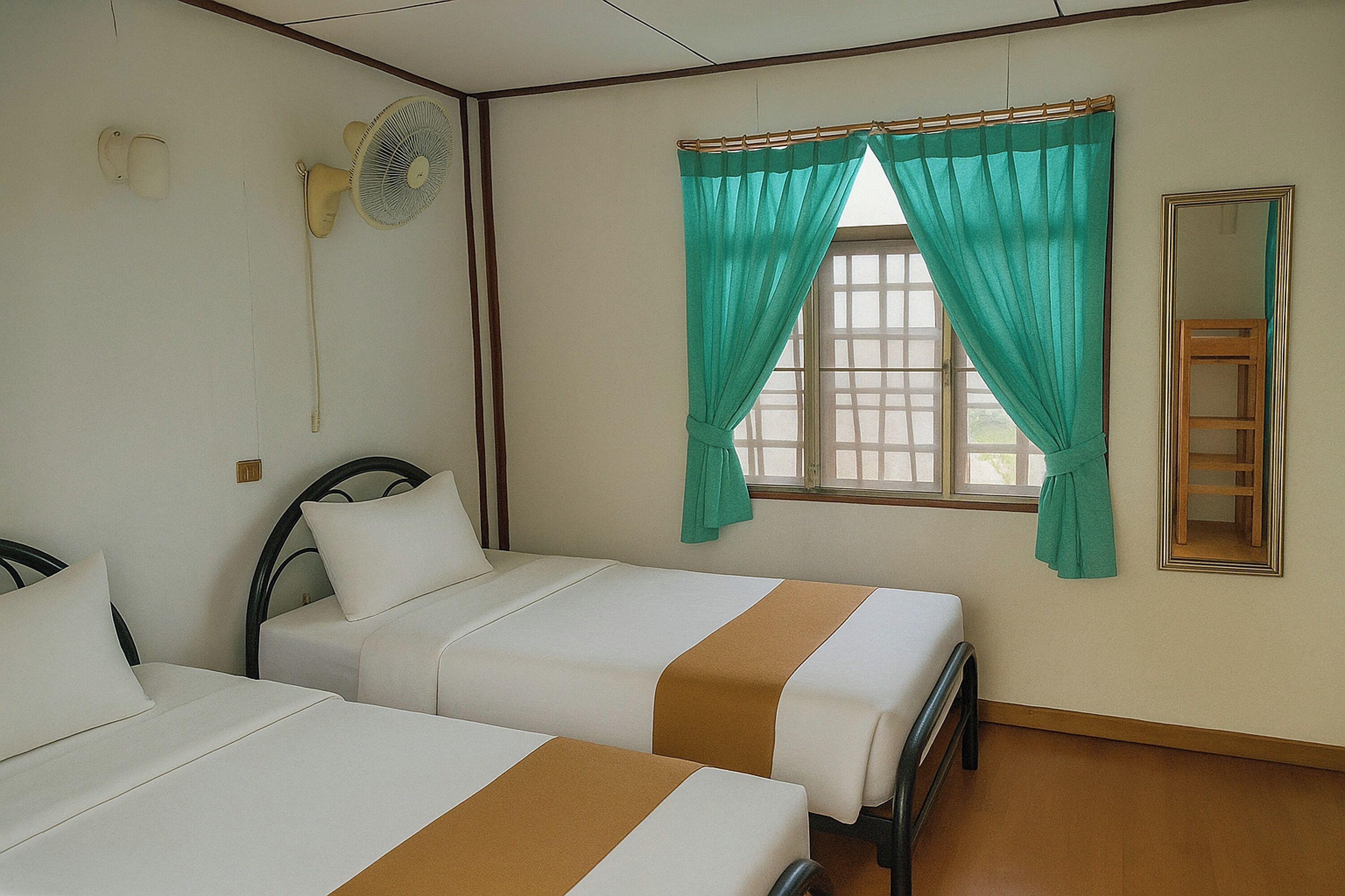Een hotelkamer met twee bedden, een raam met gordijnen, een ventilator en een spiegel.