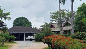 A covered parking area with a white pickup truck, surrounded by lush greenery and a large tree. - Palm Point Village (Koh Samui)