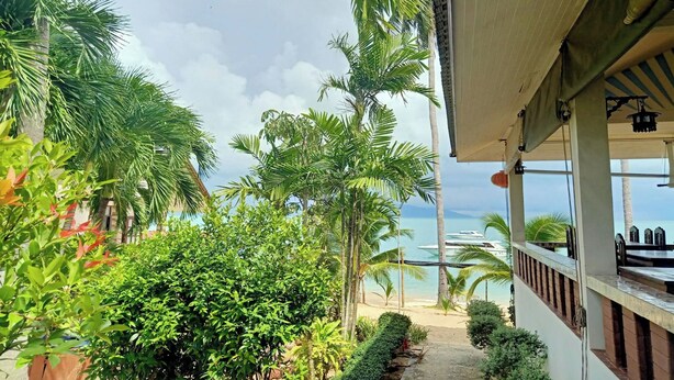 A view of a beach with palm trees and a pathway leading to a building with a balcony overlooking the sea. - Palm Point Village (Koh Samui)