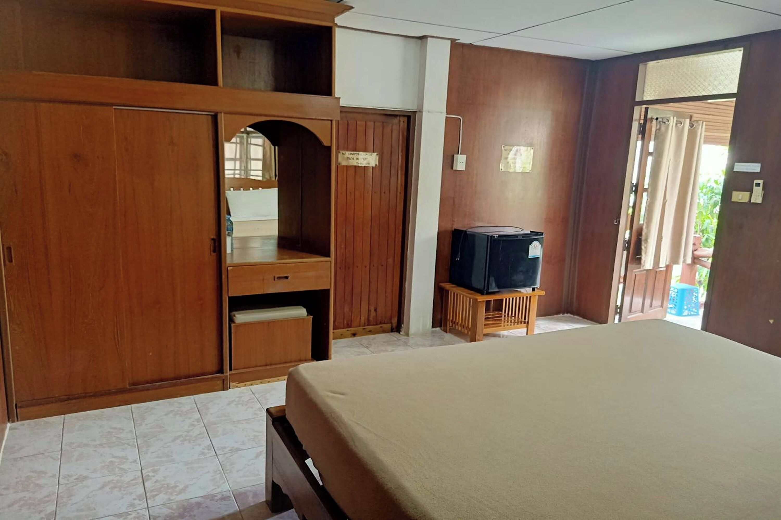 Una camera d'albergo con un letto, un armadio in legno, una televisione su un tavolino e una porta che dà sull'esterno.