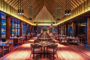 Un comedor amplio y luminoso con mesas y sillas largas, ventanas grandes y un techo alto con vigas de madera.