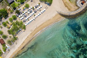 An aerial view of a beach with a circular stone wall, umbrellas, and lounge chairs. - The Sakala Resort Bali (Nusa Dua)