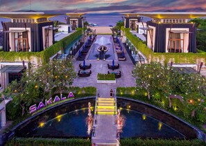 A modern hotel with a central pool, outdoor seating, and a view of the sea. - The Sakala Resort Bali (Nusa Dua)