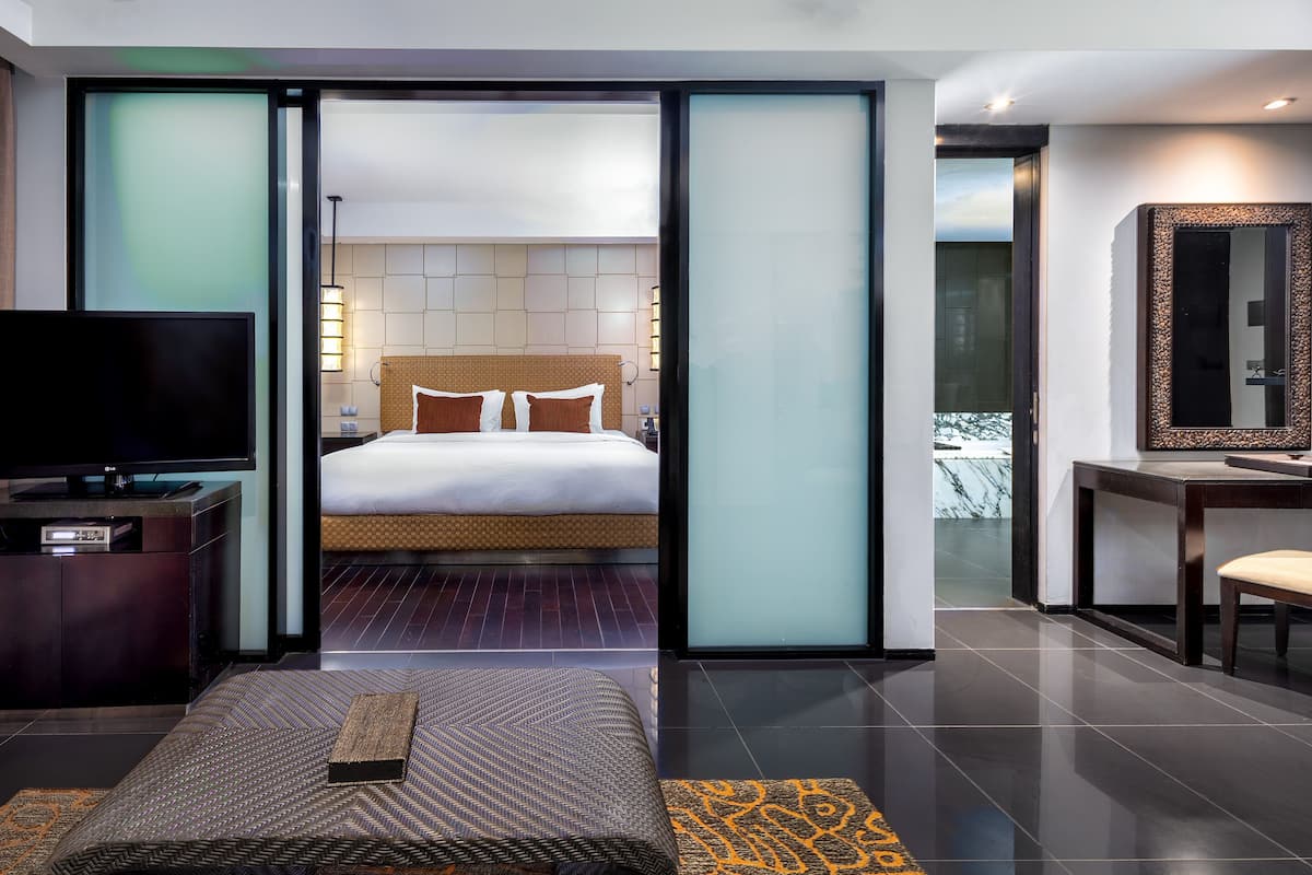 Ein modernes Hotelzimmer mit einem großen Bett, einem Fernseher, einem Schreibtisch und einem durch eine Glastür einsehbaren Badezimmer.