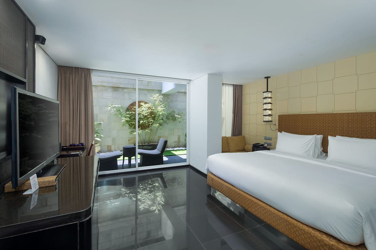 Ein modernes Hotelzimmer mit einem großen Bett, einem Fernseher und einem Balkon mit Blick auf Grünflächen.
