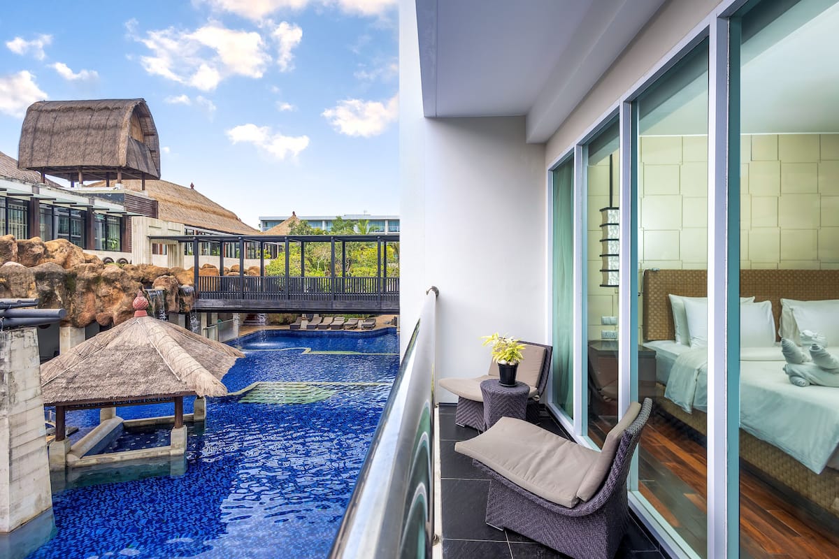 Ein Balkon mit Pool, eine strohgedeckte Struktur und ein Bett mit weißer Bettwäsche.