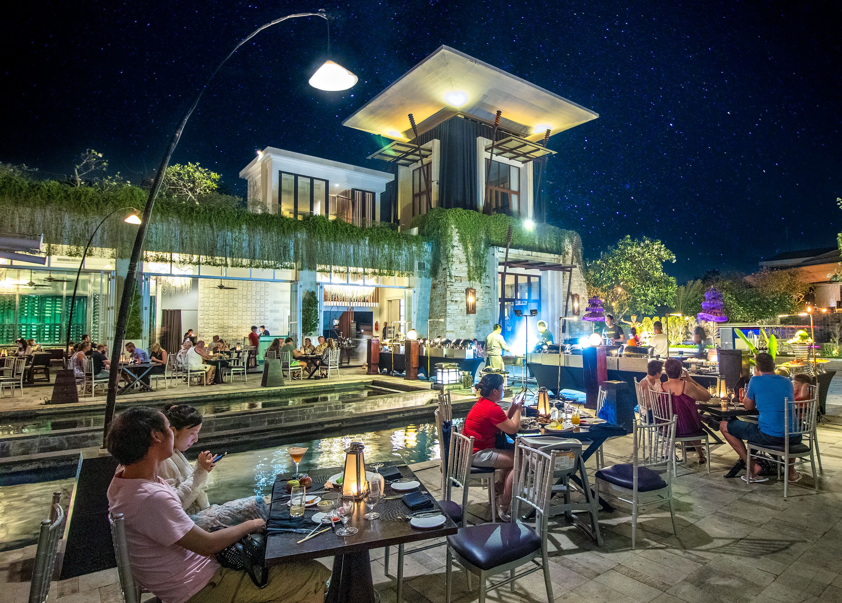 An outdoor dining area with tables and chairs, a water feature, and a building with a modern design.