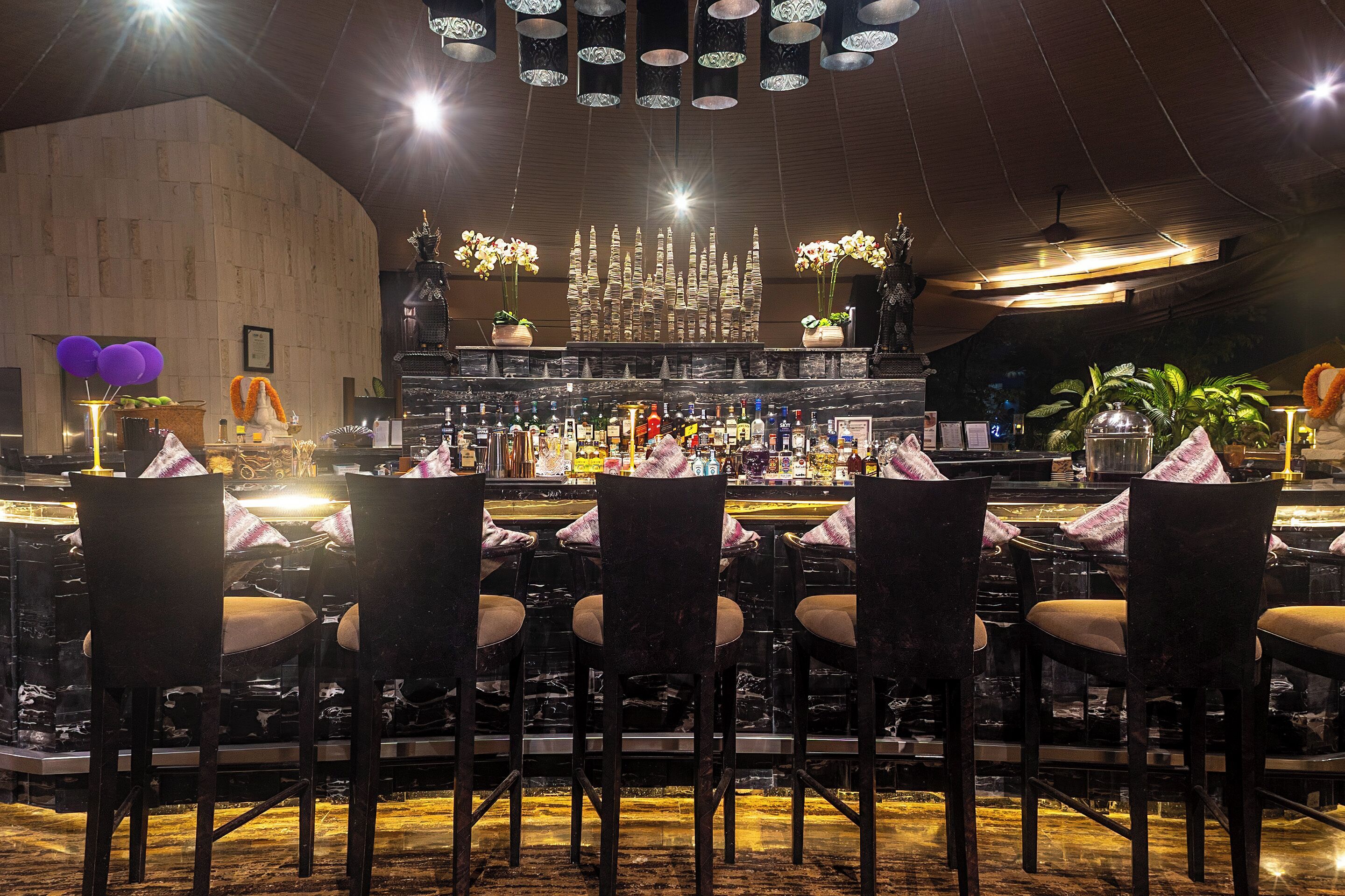 Een barruimte met meerdere stoelen en tafels, een bar met verschillende flessen en een decoratieve kroonluchter.