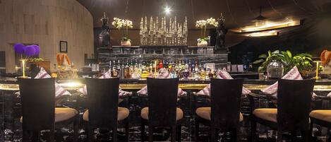 A bar area with multiple chairs and tables, a bar counter with various bottles, and a decorative chandelier.