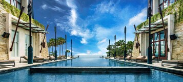 Una piscina infinita con vista despejada al océano, rodeada de sillones de descanso y arquitectura moderna.
