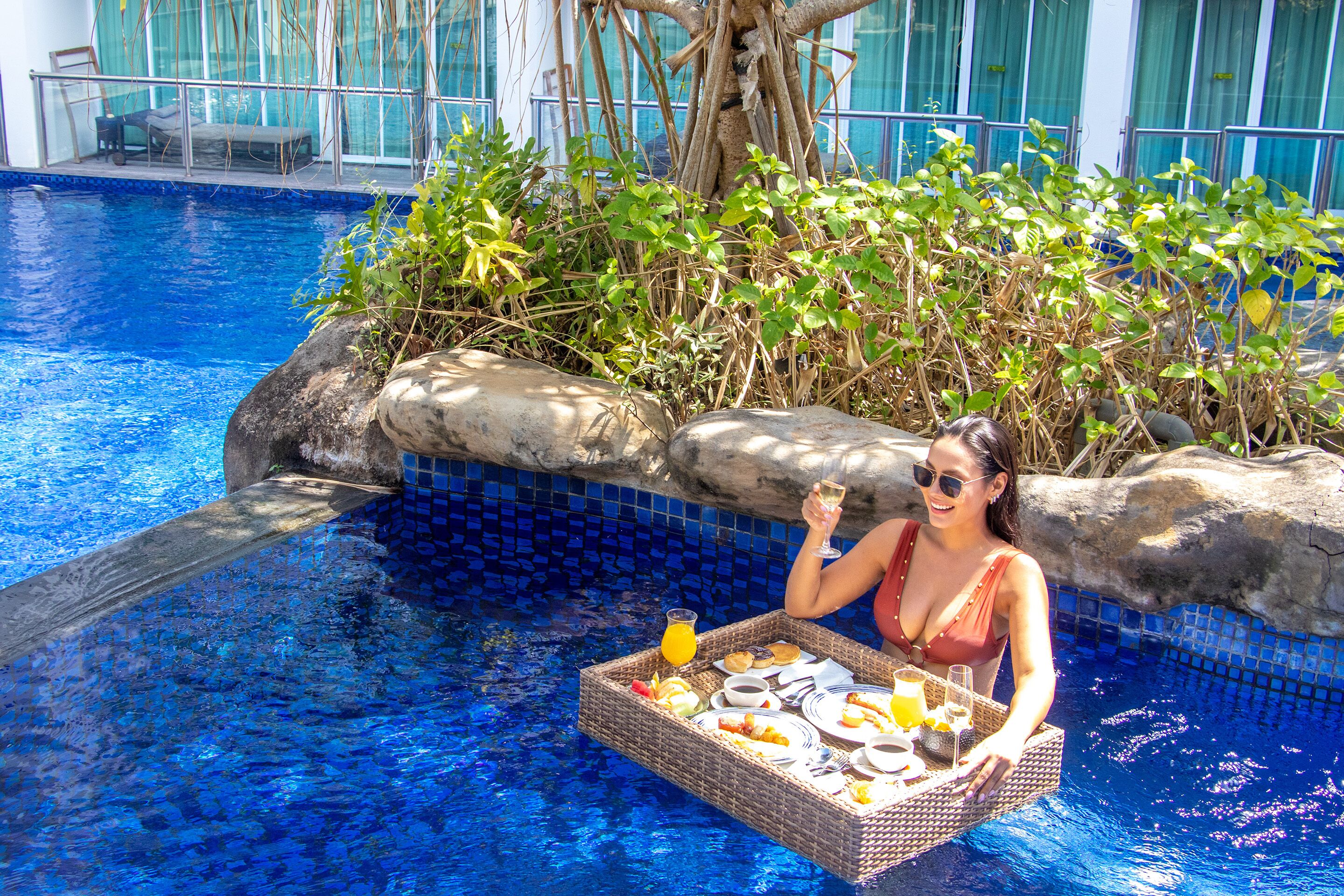 A poolside setting with a tray of breakfast items, a glass of orange juice, and a person holding a glass.