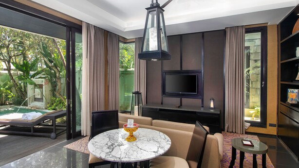 A modern hotel room with a pool, a sofa, a dining table, and a TV.