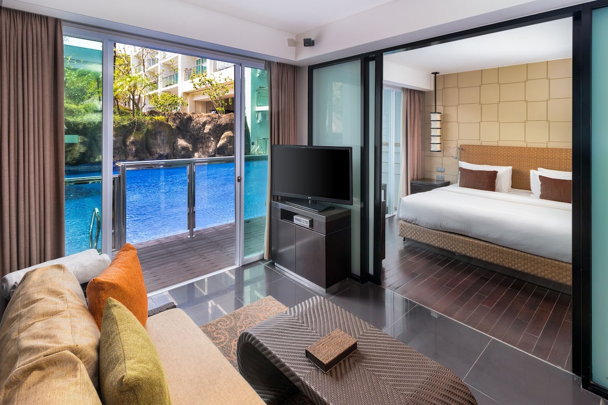 Ein modernes Hotelzimmer mit Balkon, Bett, Fernseher und Blick auf Pool und Grünflächen.