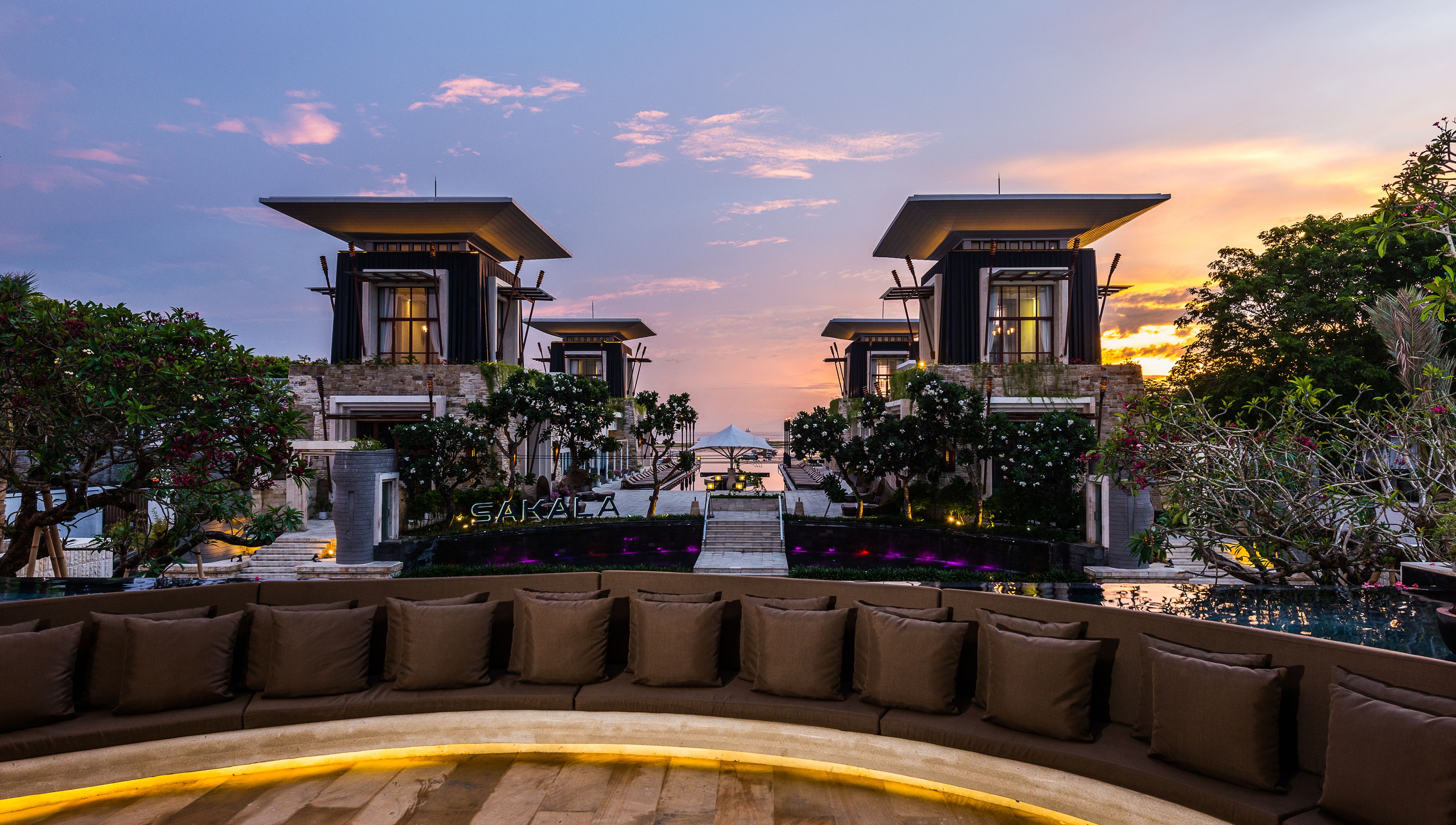 Un hotel moderno con zona de piscina, asientos exteriores y vistas al atardecer.