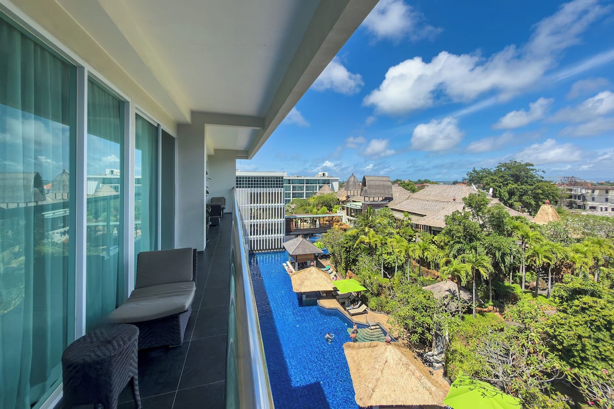 Ein Balkon mit Blick auf einen Swimmingpool, Liegestühle und ein modernes Gebäude im Hintergrund.