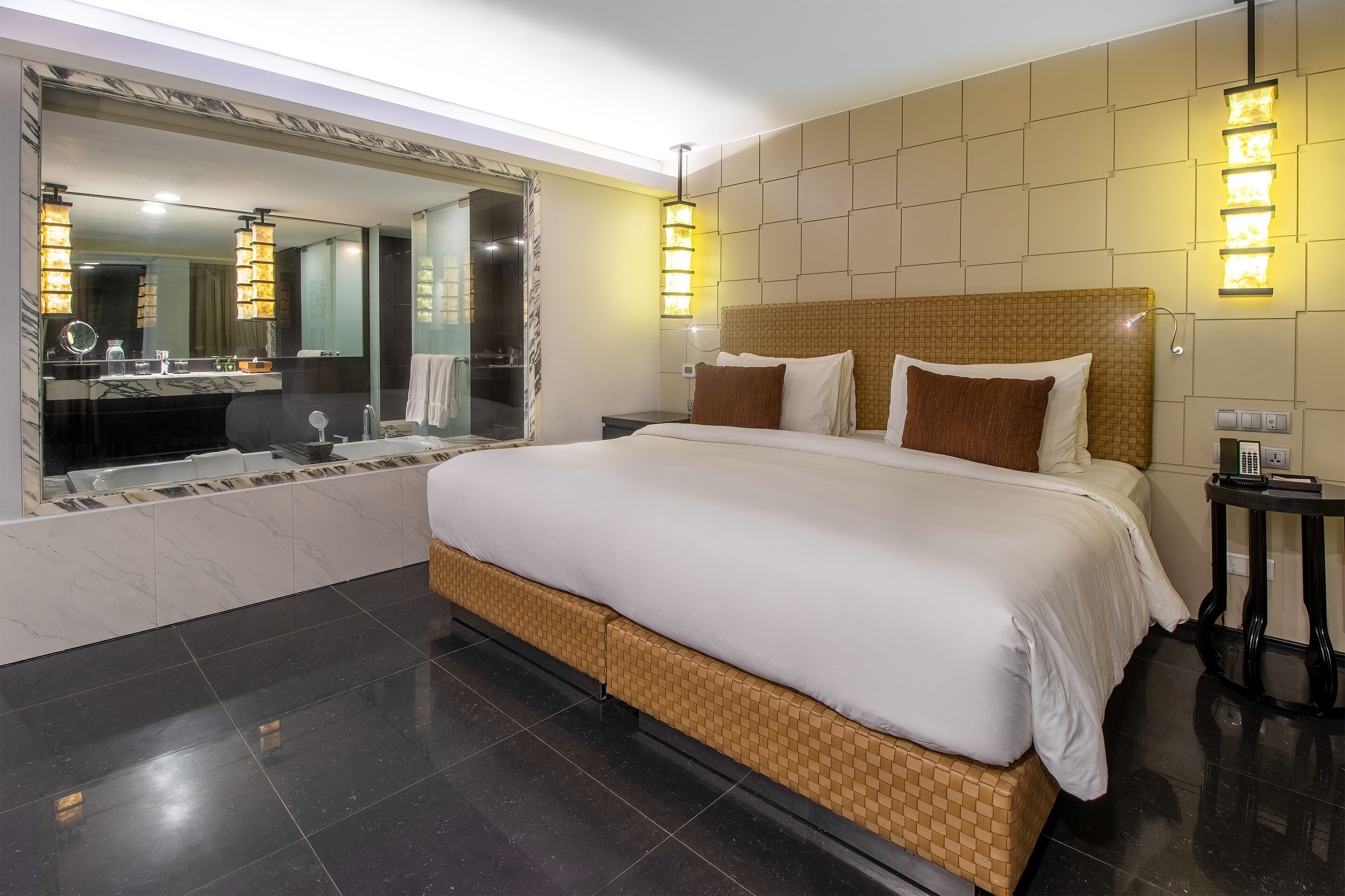 Quarto de hotel moderno com uma cama grande, banheiro com toucador e um espelho amplo.