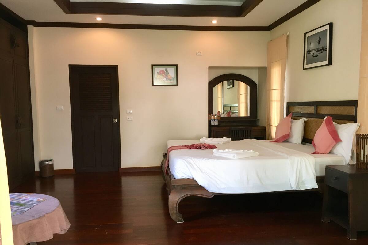 A hotel room with a large bed, a bedside table, a dresser, a mirror, and a door.