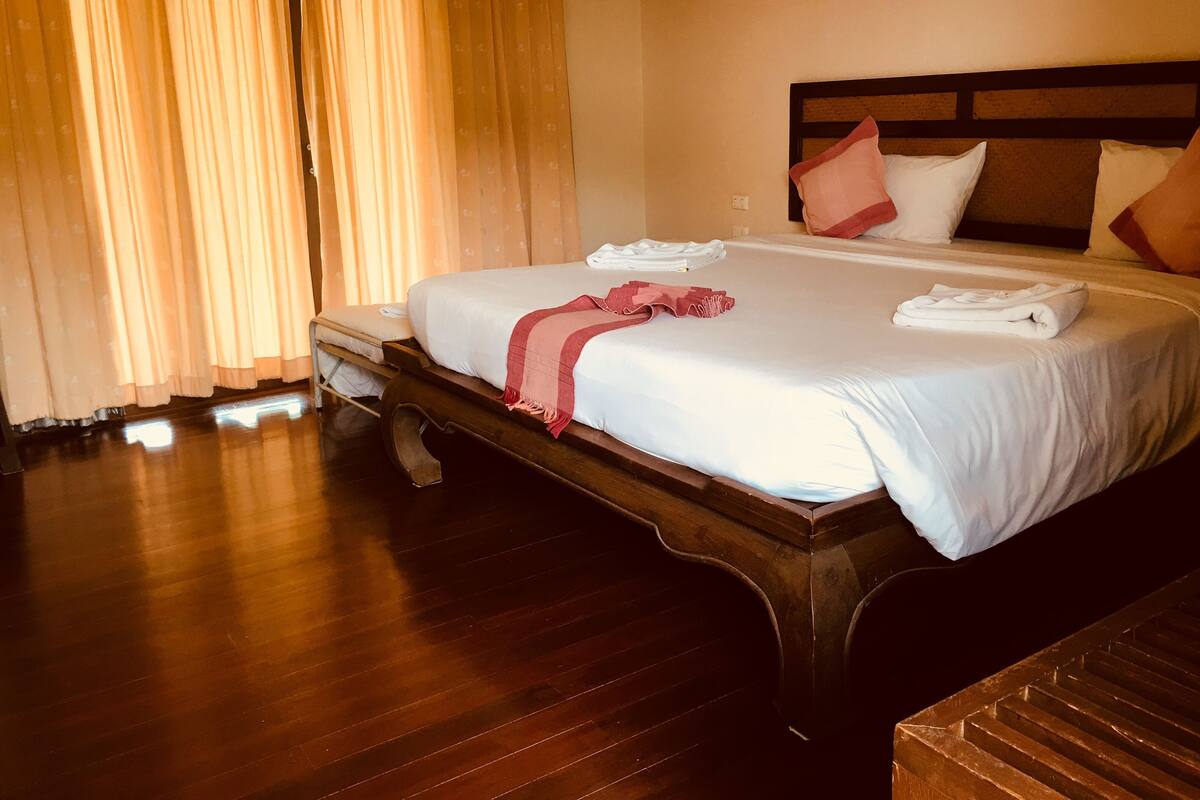 A hotel room with a large bed, wooden headboard, and a wooden bench.