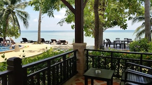 A poolside area with lounge chairs and a table, overlooking a beach and the sea. - Grand Manita Beach Resort (Koh Samui)