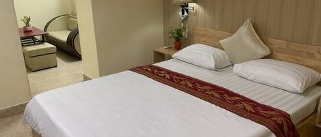 A hotel room with a large bed, a bedside table with a lamp, a chair, and a small table with a plant.
