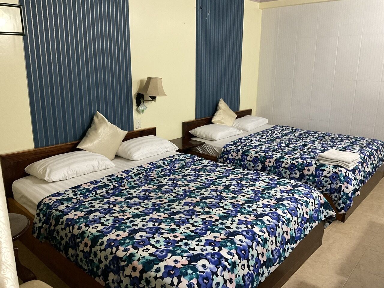 Une chambre d’hôtel avec deux lits, chacun recouvert d’une couvre-lit à motifs floraux, agrémenté d’oreillers blancs et doté d’une tête de lit en bois.