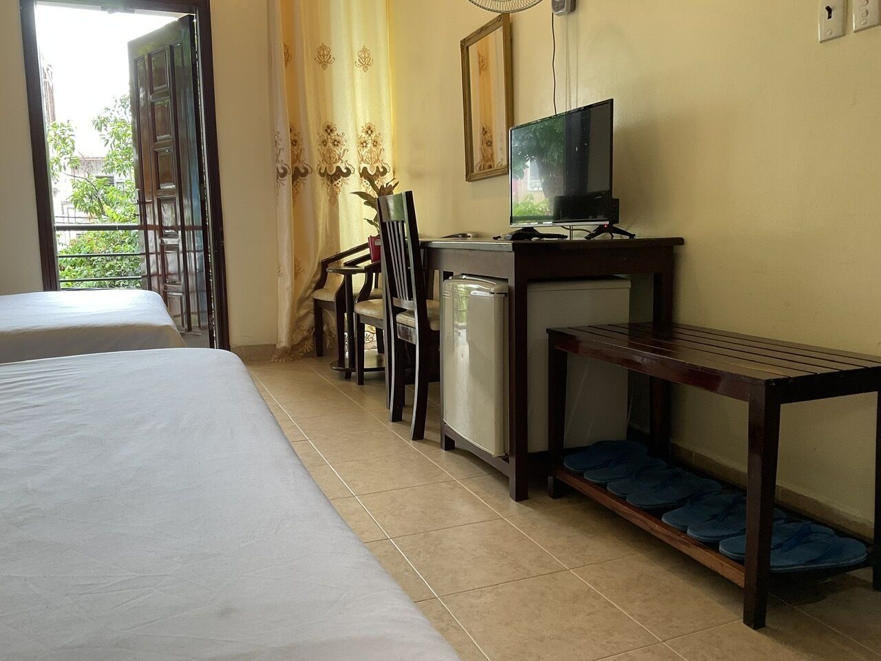 A hotel room with two beds, a desk with a television, a small refrigerator, and a chair.