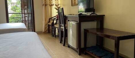 A hotel room with two beds, a desk with a television, a small refrigerator, and a chair.