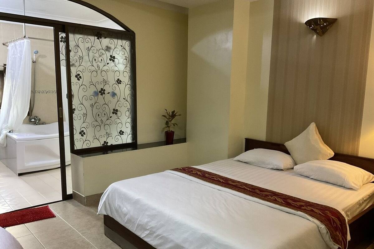Une chambre avec un grand lit, un espace douche, une plante en pot et un panneau décoratif mural.