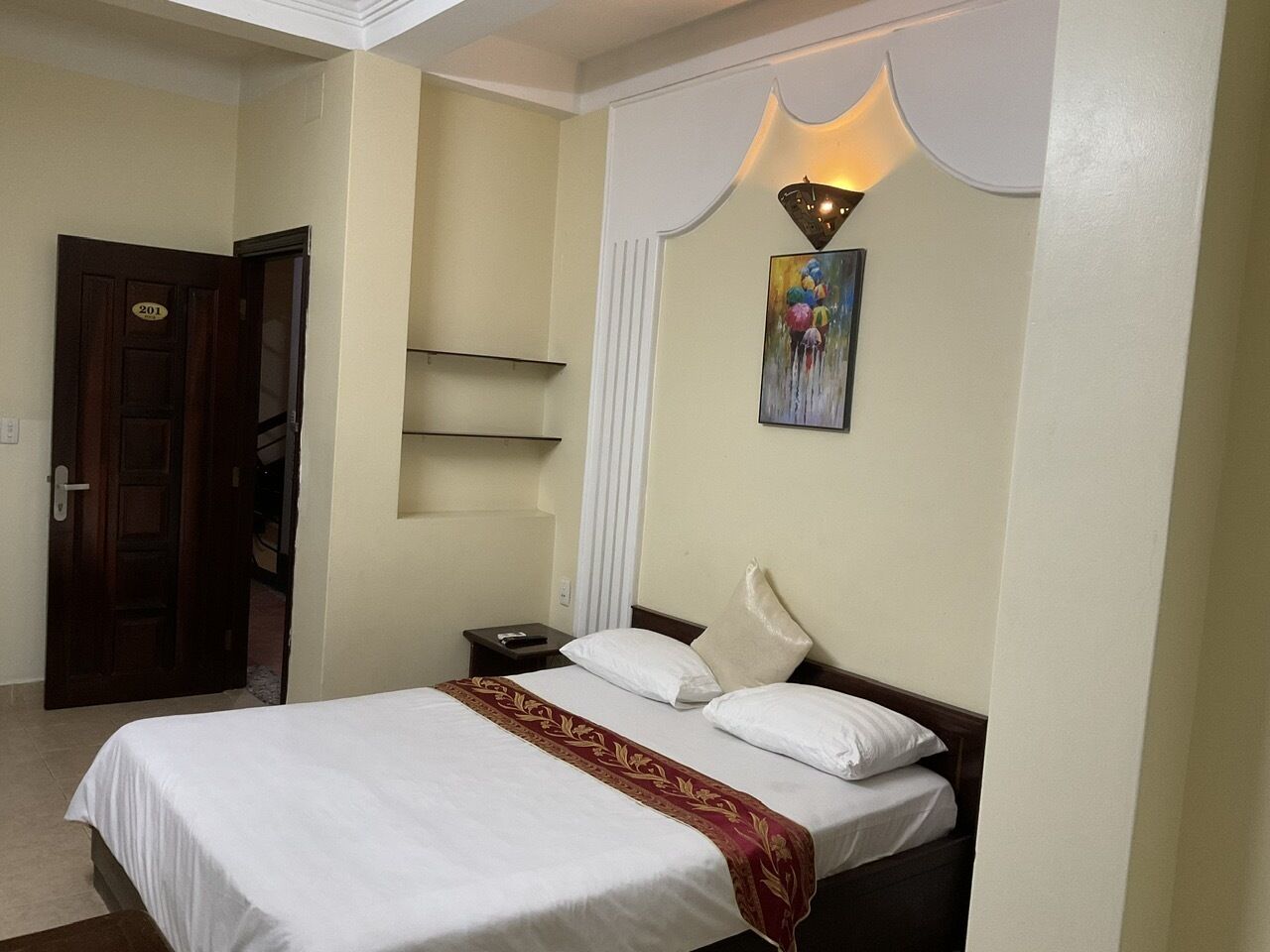 Habitación de hotel con una cama, una mesita de noche, una lámpara de pared y una puerta.