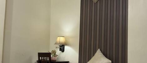 Una habitación de hotel con cama, mesita de noche, lámpara e iluminación en la pared.