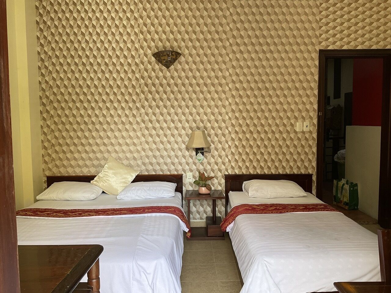 Habitación de hotel con dos camas, una mesita, una lámpara y un papel tapiz estampado.