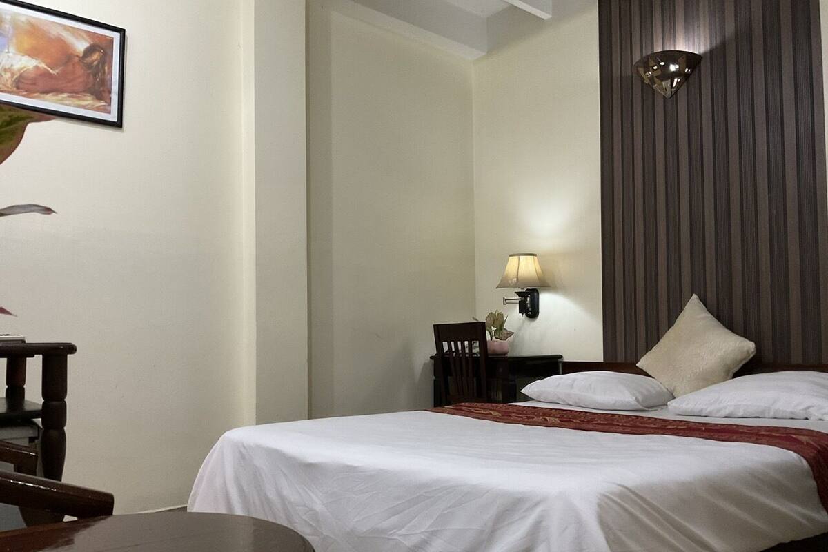 Une chambre d’hôtel avec un lit, un bureau, une chaise, une lampe et un tableau au mur.