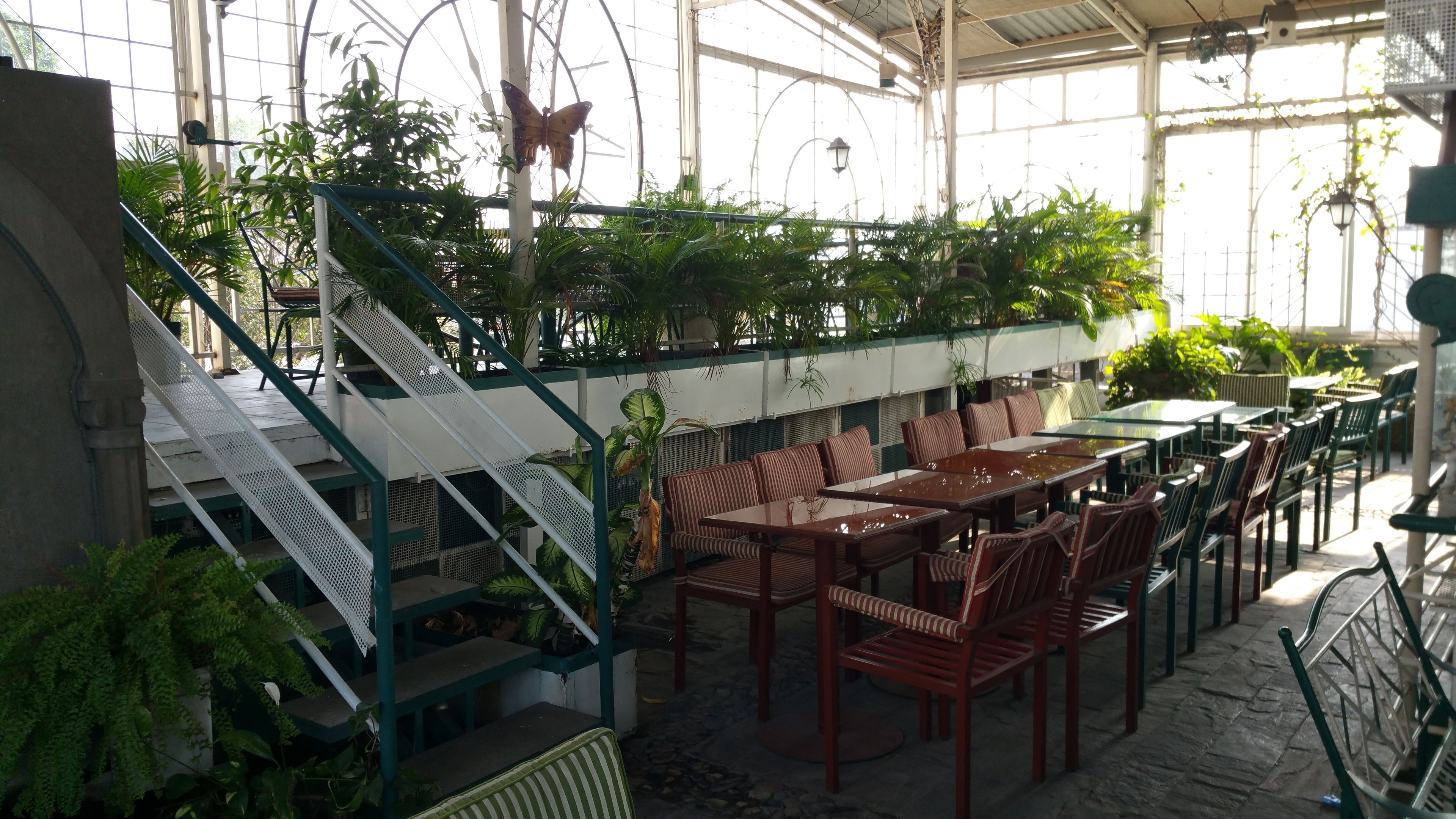 An indoor restaurant with a staircase, tables, chairs, and hanging plants.