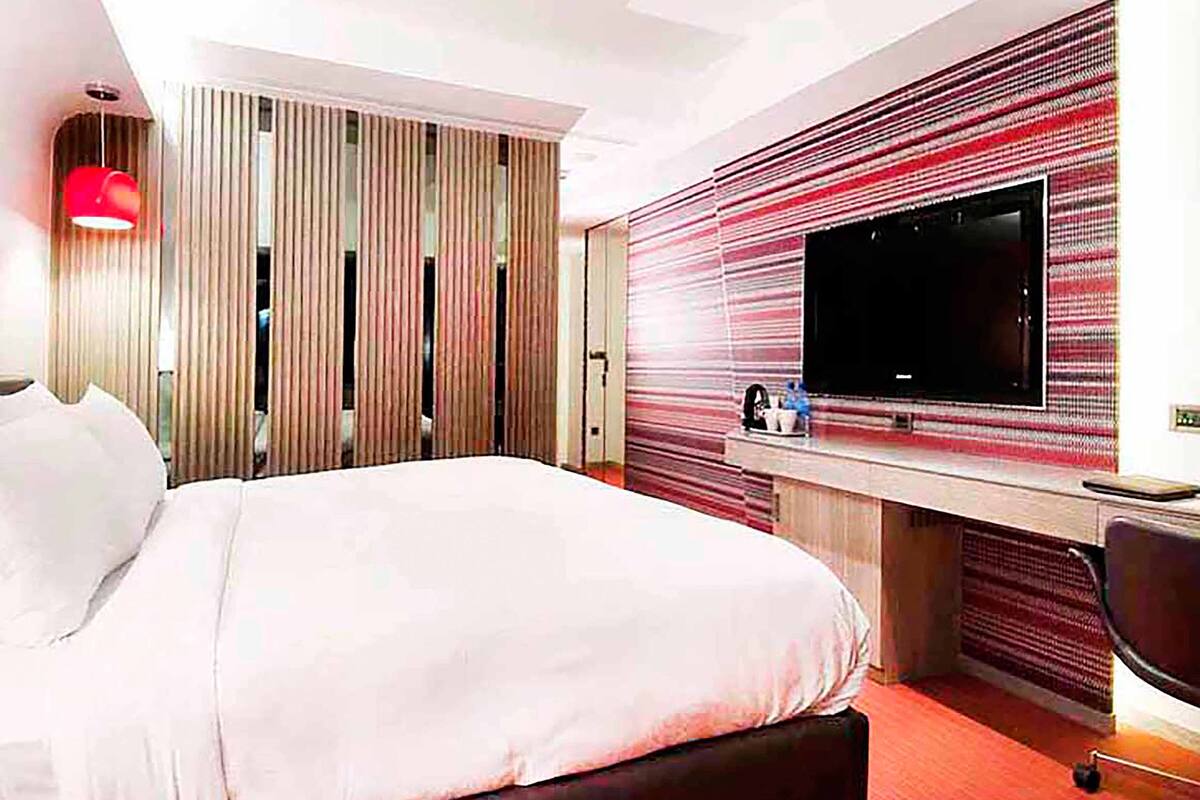 Habitación de hotel con una cama grande, un televisor montado en la pared y un escritorio con una silla.