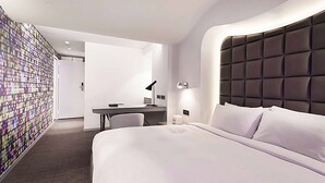 A modern hotel room with a large bed, a desk, and a chair.