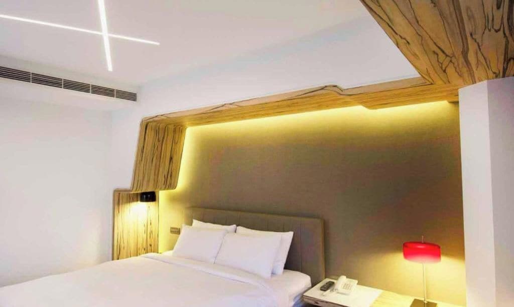 A modern hotel room with a large bed, a wooden headboard, a bedside table with a lamp, and a phone.