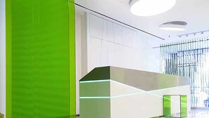 A modern reception area with a green accent wall, a reception desk with illuminated edges, and a ceiling with circular light fixtures.