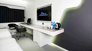 A modern hotel room with a large TV, a desk with a coffee maker, and a comfortable seating area.