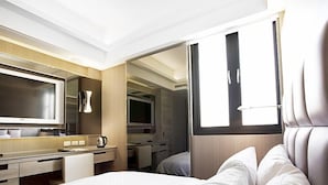 Ein modernes Hotelzimmer mit Bett, Schreibtisch, Fernseher und einem durch eine offene Tür einsehbaren Badezimmer.