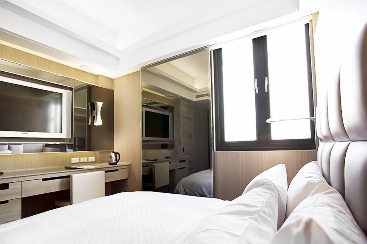 Une chambre d’hôtel moderne, équipée d’un lit, d’un bureau, d’une télévision et d’une salle de bain visible à travers une porte ouverte.