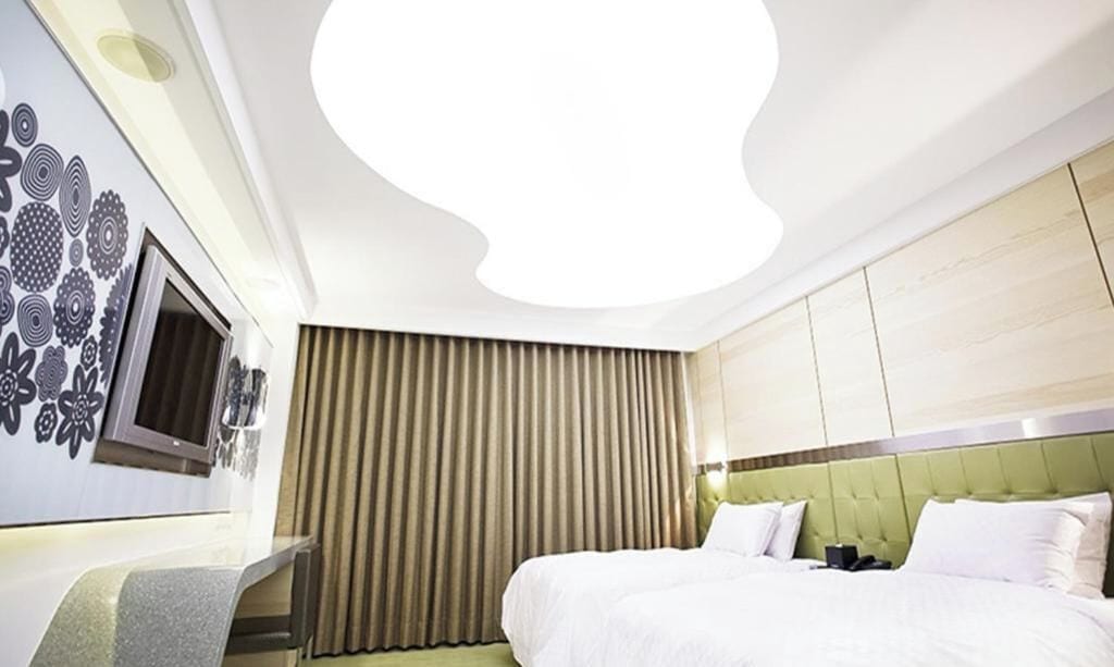 A hotel room with a bed, a TV, a desk, and a large window with curtains.