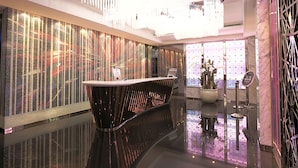 Eine moderne Hotellobby mit spiegelndem Boden, einer Rezeption und einer Wand mit vertikalen Linien.