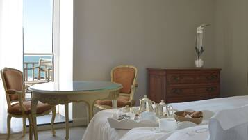 Habitación de hotel con balcón, una mesa de comedor, una silla, cómoda y cama con cubrecama blanco.