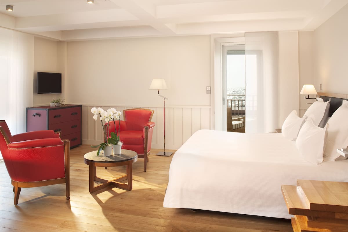 Habitación de hotel con una cama grande, un escritorio, una silla roja, una mesita con una planta y un televisor en la pared.