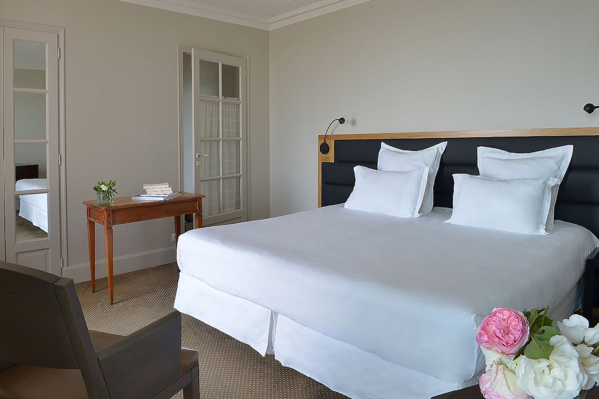 Una cama bien hecha con sábanas blancas, una mesita de noche con un florero y una puerta con paneles de vidrio esmerilado.